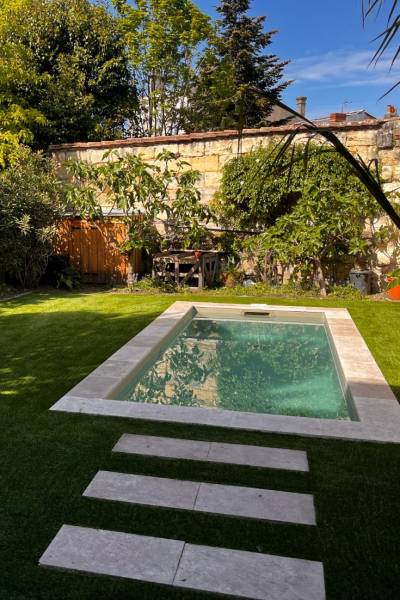 Un design épuré et une luminosité maximale grâce au contraste des margelles beiges sur cette piscine béton armé parfaitement intégrée au jardin.